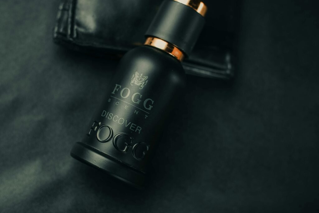 Close-up of a Fogg perfume bottle on a black surface with a leather wallet.